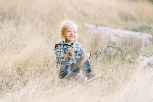Little happy girl sits in dry grass on the lawn photo