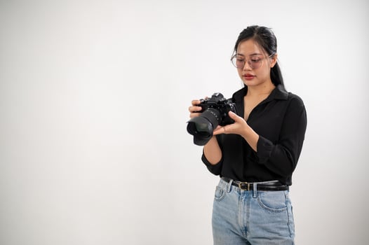 A confident, experienced Asian female photographer is adjusting her DSLR camera, preparing photoshoot equipment, and working in the studio. photo