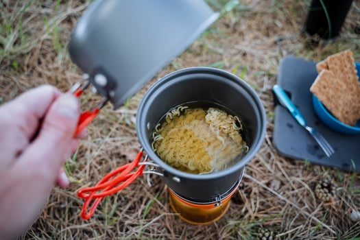 Tourist utensils, camp cooking in a pot, open the lid look inside the pot, cook noodles, a quick meal in nature, lunch in the forest on the grass, trekking in the mountains photo