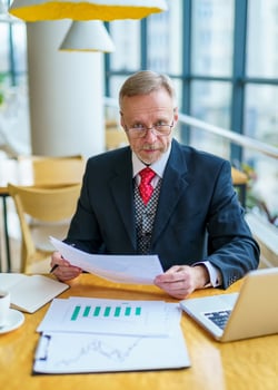 Elderly businessman using laptop and taking notes working while sitting in modern office. Selective Focus photo