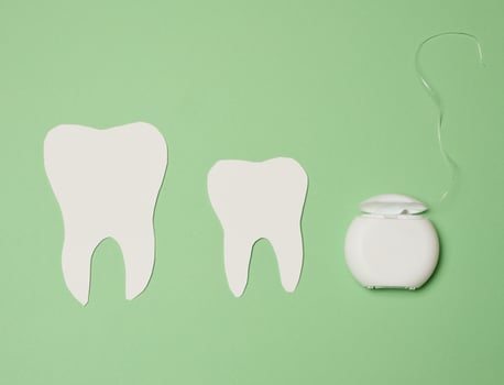 Dental floss and paper teeth on green background, oral hygiene photo