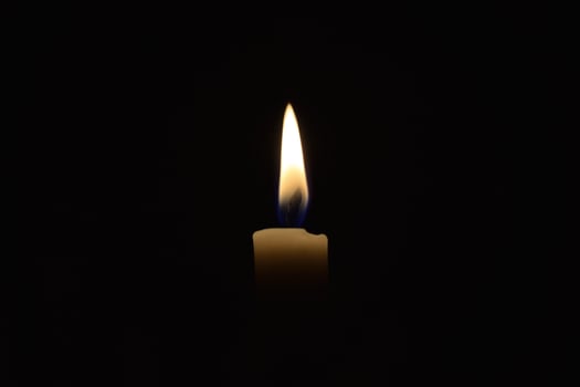 Single Candle with flame in the dark place, isolated black background photo