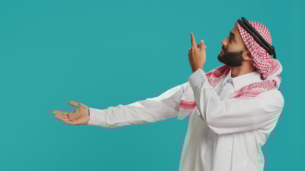 Confident muslim man in traditional clothes showing with hands at copyspace for advertisement commercial in studio. Smiling islamic person showcasing to side with arms and looking at camera. photo