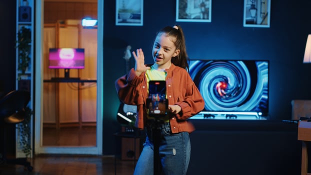 Young girl dancing in dimly lit home studio interior, producing content with mobile phone. Smiling child doing viral dance choreography in living room with 3D animations on monitors in background photo