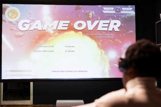 Gamer wearing headphones upset at seeing game over message on widescreen TV while playing arcade space shooter videogame. Man relaxing at home on gaming system, disappointed after losing photo