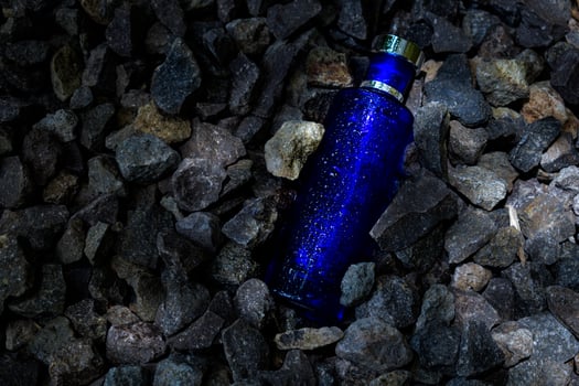 Perfume Dark Blue transparent bottle in gravel or coral background photo