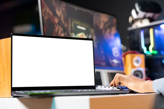 Focus on isolated screen laptop on desk next to player playing singleplayer videogame in neon lit apartment. Close up shot of mockup notebook and man enjoying game on computer photo