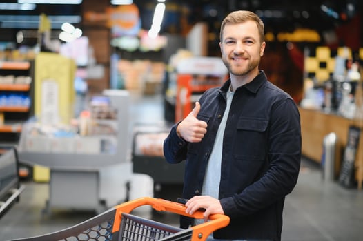 Customer In Supermarket. Man Doing Grocery Shopping Standing With Cart Choosing Food Product Indoors. Guy Buying Groceries In Food Store. Selective Focus, Copy Space. photo
