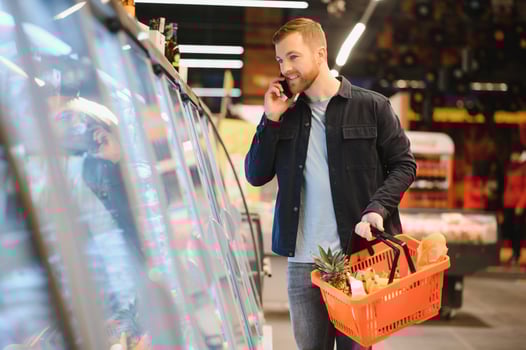 Young man buying groceries at the supermarket. Other customers in background. Consumerism concept. photo