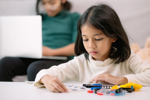 A young girl is sitting at a table with a laptop and a stack of Legos photo