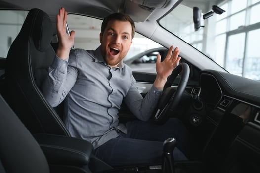 Happy young driver behind the wheel inside new car. Lifestyle scene in the car dealership photo