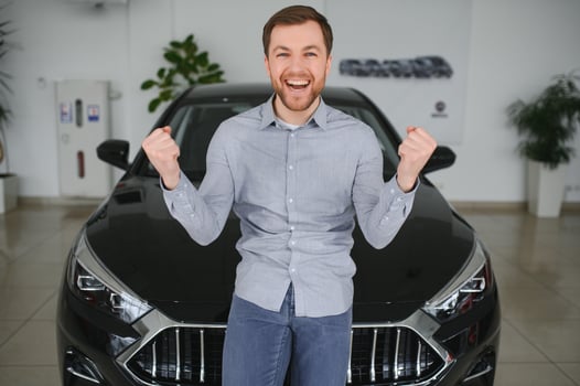 Emotional handsome guy raising hand up and smiling at camera. Rich man buying auto at luxury dealership salon photo