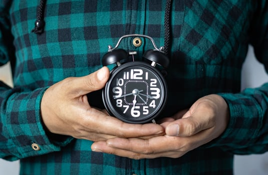 Time management concept. Man hands holding Black retro alarm clock. Time to wake up for the morning routine photo