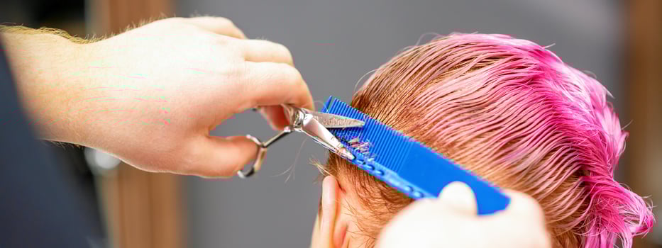 Professional hairstylist is cutting short pink hair with scissors in hair salon close up. photo