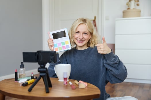 Portrait of young smiling woman, girl reviewing palette eyeshadow, shows thumbs up, recording blog, vlogging in her room, recommending makeup product photo