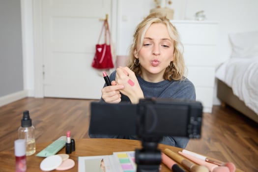 Portrait of young female blogger, beauty makeup vlogger, showing lipstick swatches on her hand, recommending cosmetics to her followers, creating content for social media account on digital camera photo