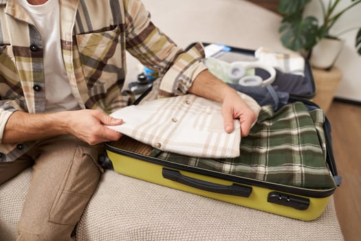 Cropped shot of male hands putting clothes inside suitcase, packing for business work trip or going on vacation, getting ready for holiday journey, preparing luggage photo