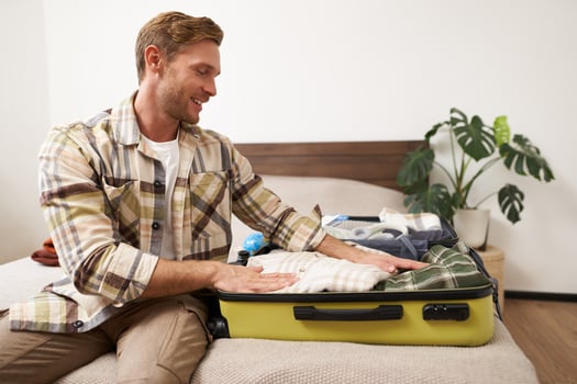 Portrait of handsome young man going on holiday, guy prepares for a trip journey, packs his suitcase, puts clothes in luggage, gets ready for adventure photo