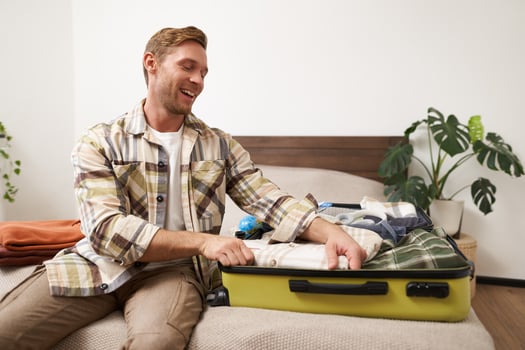 Portrait of cheerful young man preparing for summer holiday, going on vacation, packing his suitcase with clothes and smiling excited photo