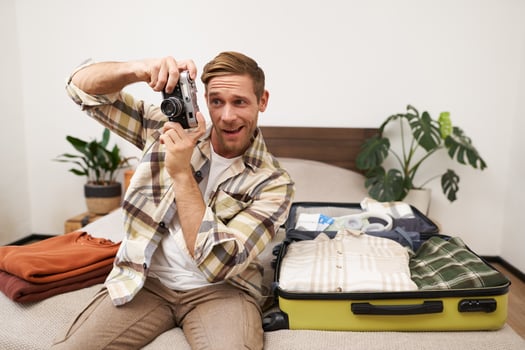 Portrait of handsome man going on vacation, packing suitcase, holding camera, travel photographer going on holiday photo