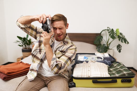 Portrait of handsome happy man, holding his analogue camera, sitting near opened suitcase, packing things for holiday, travelling abroad, getting ready for vacation photo