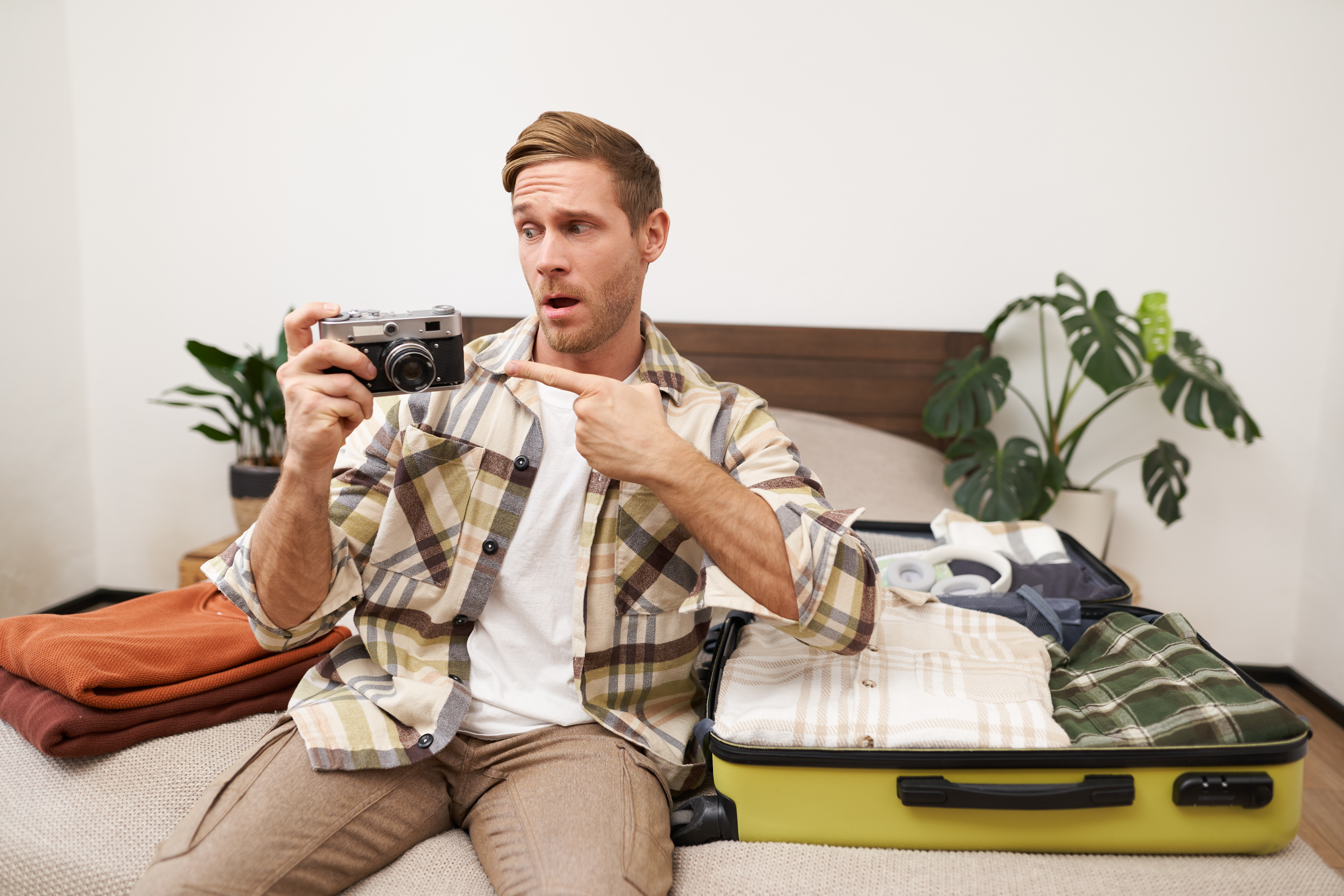 Portrait of handsome happy man, holding his analogue camera, sitting near opened suitcase, packing things for holiday, travelling abroad, getting ready for vacation photo