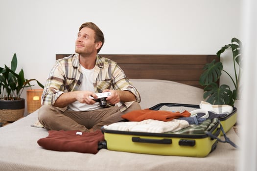 Portrait of tourist, man sits with suitcase on bed, holds camera, packs suitcase with clothes, goes on holiday, prepares for summer vacation, tourist travels abroad photo