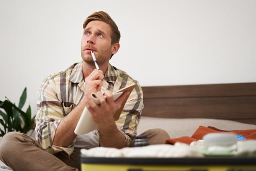 Portrait of thoughtful young man, tourist going on vacation, going through holiday check-list, writing down what he wants to take on travelling photo