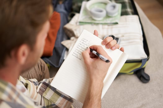 Close up portrait of man packing suitcase, making notes, check-list of items he wants to take on holiday, packing luggage photo