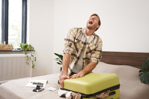 Portrait of man struggling to close suitcase full of clothes, putting effort to pack luggage for holiday, going on long vacation with lots of things photo