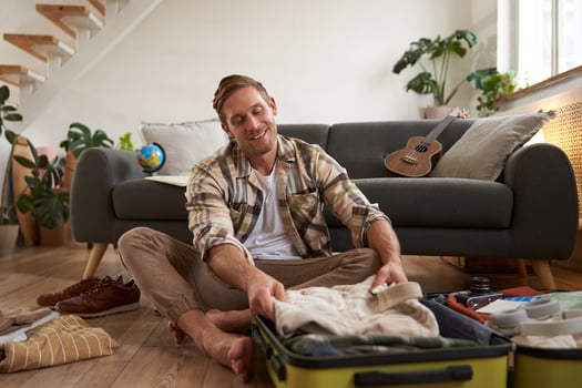 Travelling and tourism concept. Happy young man, sits on floor with luggage opened, packing suitcase for holiday, going on vacation, putting clothes inside a bag photo