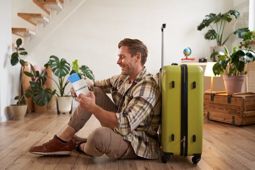 Portrait of handsome young man, tourist sitting with his suitcase, holding passport and flight tickets, going on holiday photo