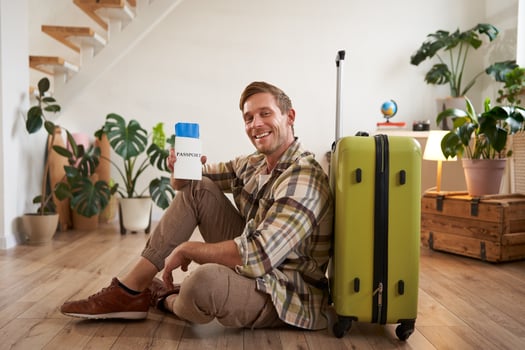 Smiling handsome guy looks at his passport and flight ticket, sits on floor with suitcase photo