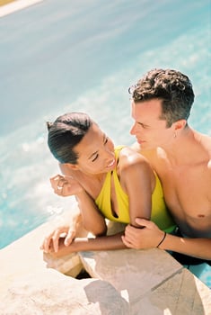 Man hugs smiling woman from behind and looks at her, leaning on the side of the pool photo