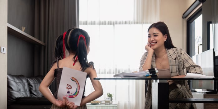 Happy family, mother and little daughter hold drawings for mom to see, sitting in cozy room at home. Working mom work from home office photo
