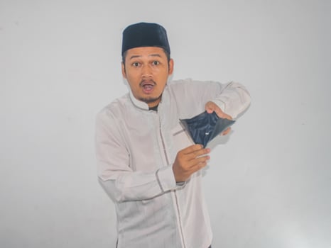 Asian muslim man showing empty wallet with shocked face expression photo