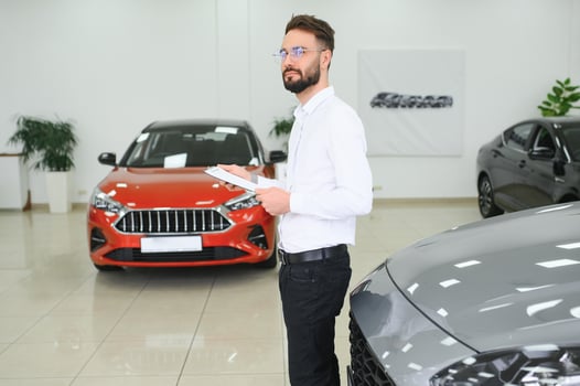 Confident young caucasian businessman shop assistant standing in car automobile dealer shop photo