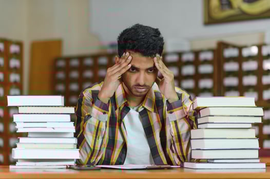 Portrait of cheerful male international Indian student with backpack, learning accessories standing near bookshelves at university library or book store during break between lessons. Education concept photo