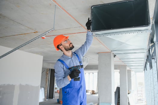 Industrial Theme. Warehouse Heating and Cooling System Installation by Professional Caucasian Technician. Commercial Building Ventilation Rectangle Canals. Air Distribution. photo
