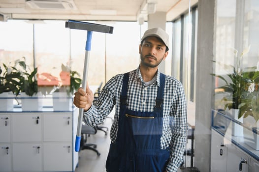 Young indian man washing window in office. photo
