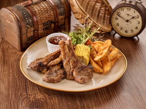 Grilled Lamb Chop, chips, salad, sauce and corn in a dish isolated on dark wooden table side view singapore food photo