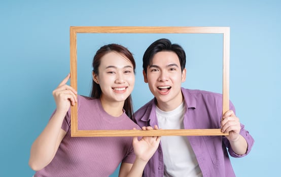 Young Asian couple holding photo frame on blue background