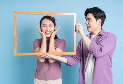 Young Asian couple holding photo frame on blue background