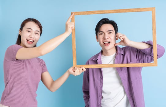 Young Asian couple holding photo frame on blue background