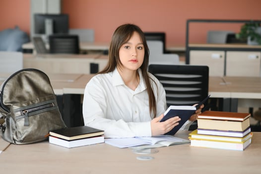 A cute 15-year-old schoolgirl sits at a school desk with notebooks and books and studies photo
