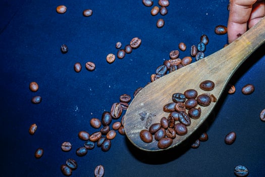 Black coffee beans are seen close up with a wooden spoon on a black cloth. photo
