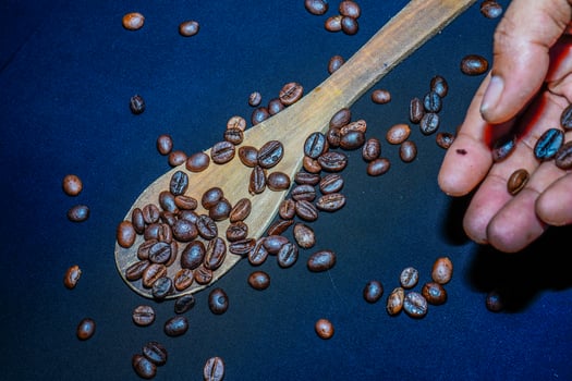 Black coffee beans are seen close up with a wooden spoon on a black cloth. photo