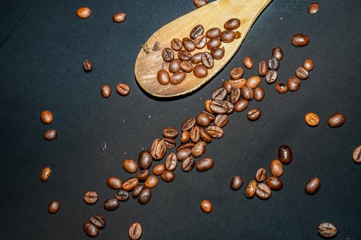 Black coffee beans are seen close up with a wooden spoon on a black cloth. photo
