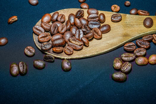 Black coffee beans are seen close up with a wooden spoon on a black cloth. photo