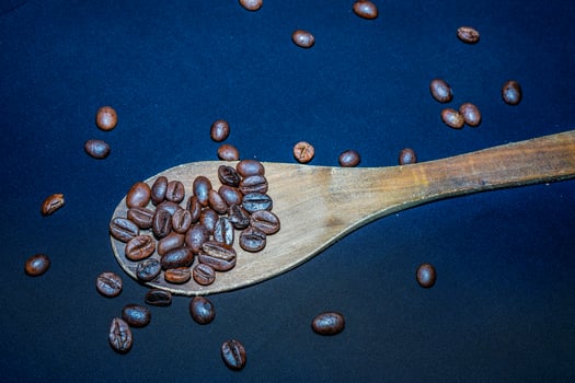 Black coffee beans are seen close up with a wooden spoon on a black cloth. photo